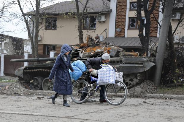 Local civilians walk past a tank destroyed during heavy fighting in an area controlled by Russian-backed separatist forces in Mariupol, Ukraine, Tuesday, April 19, 2022. Taking Mariupol would deprive Ukraine of a vital port and complete a land bridge